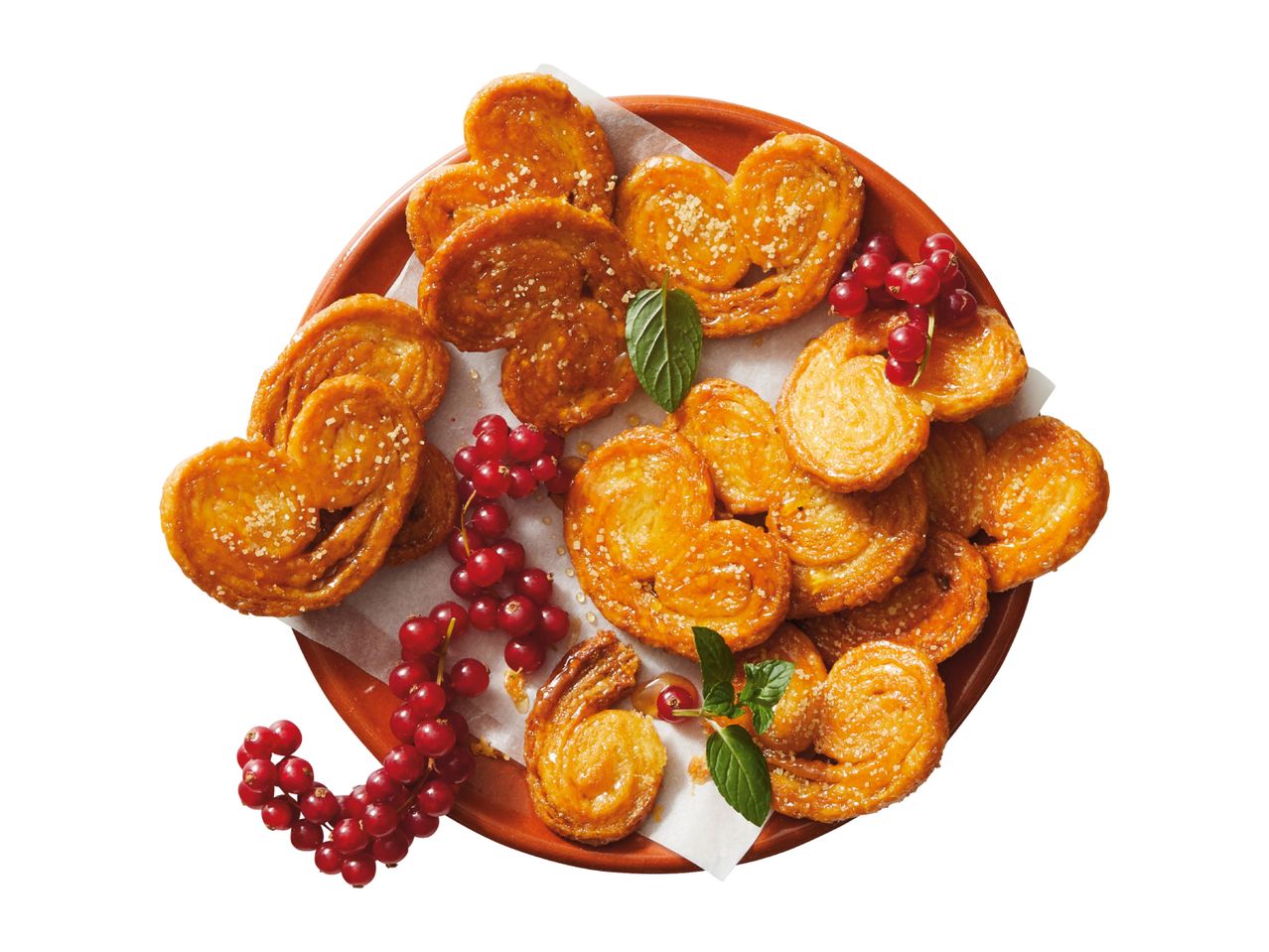 Heart-shaped puff pastry cookies with sugar, red currants, and mint on a plate.