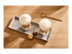 Two glasses of latte macchiato with macarons on a concrete tray on a wooden table.
