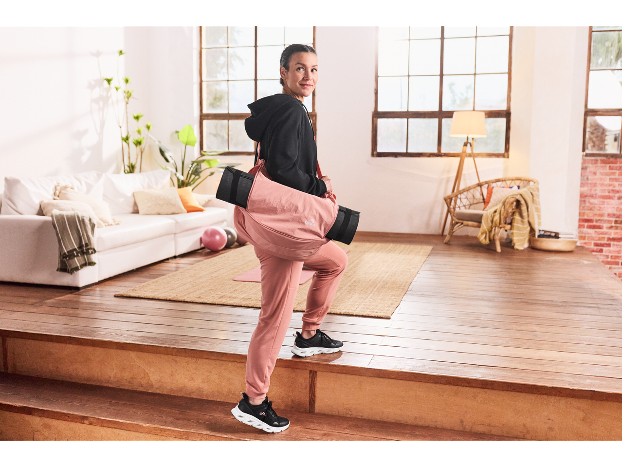 Woman in Crivit sweatshirt and sweatpants with yoga mat walking up stairs.
