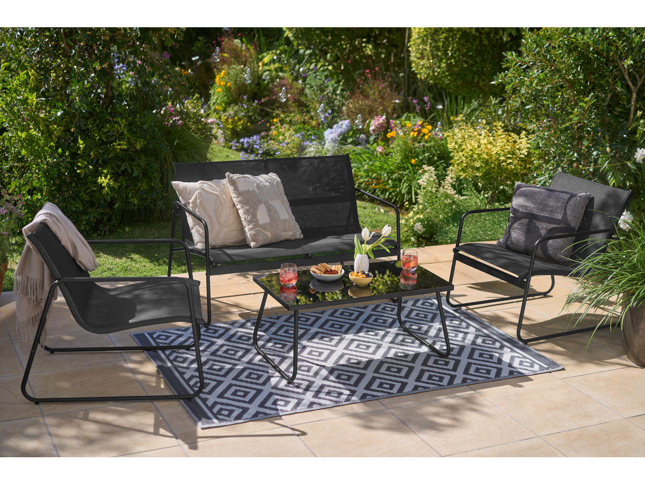 Crni vrtni namještaj s kaučem, dvije stolice i stolićem za kavu na terasi.