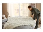 A man in plaid pajamas spreads a fluffy white blanket over a grey bed.