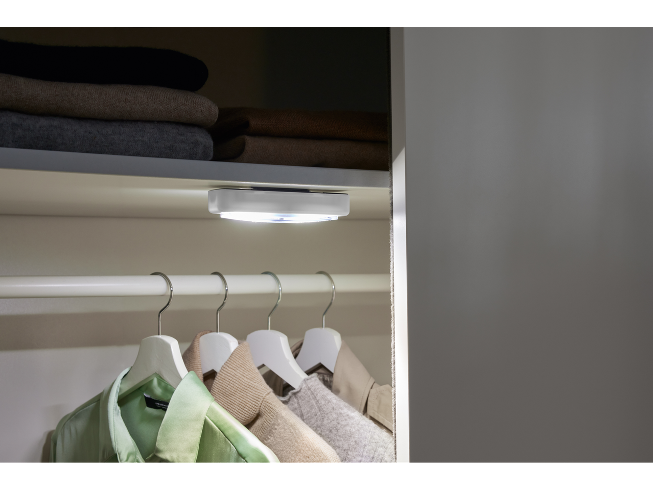 Uma pequena luz LED ilumina um armário com roupas penduradas.