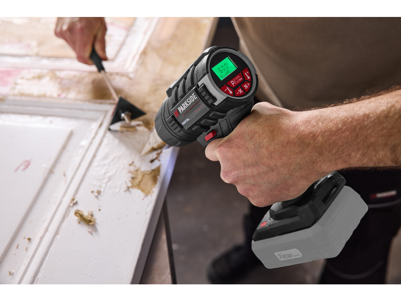Homem a usar uma pistola de ar quente sem fios PARKSIDE PERFORMANCE para decapar tinta.