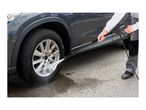 Person cleaning a car wheel with a pressure washer, showing dirty and clean parts.
