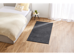 A bedroom with a bed, a side table with candles, and a gray rug on a wooden floor.