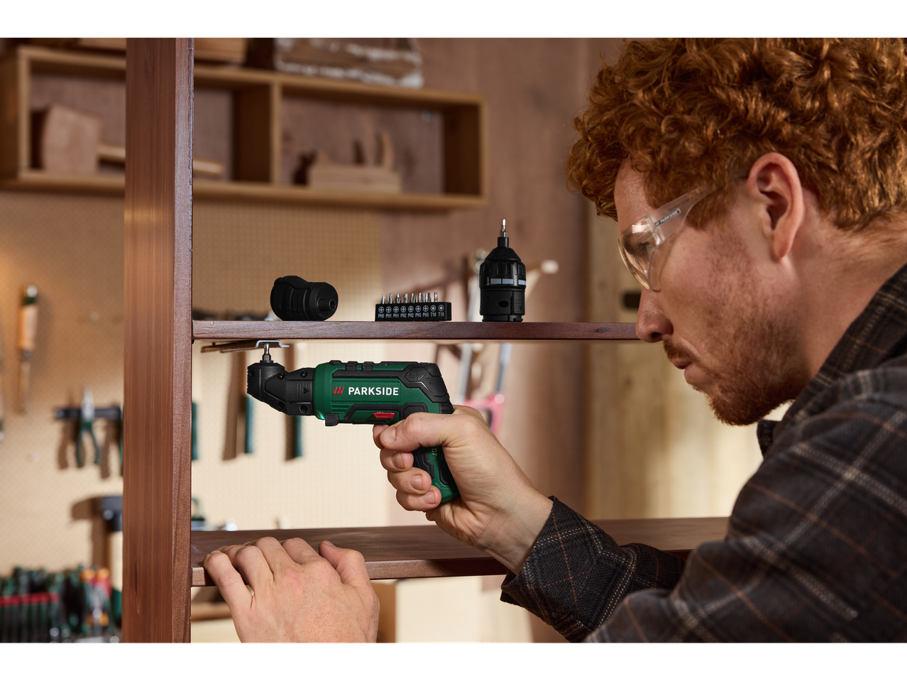 Muškarac sa zaštitnim naočalama koristi kutni odvijač za sastavljanje drvene police.