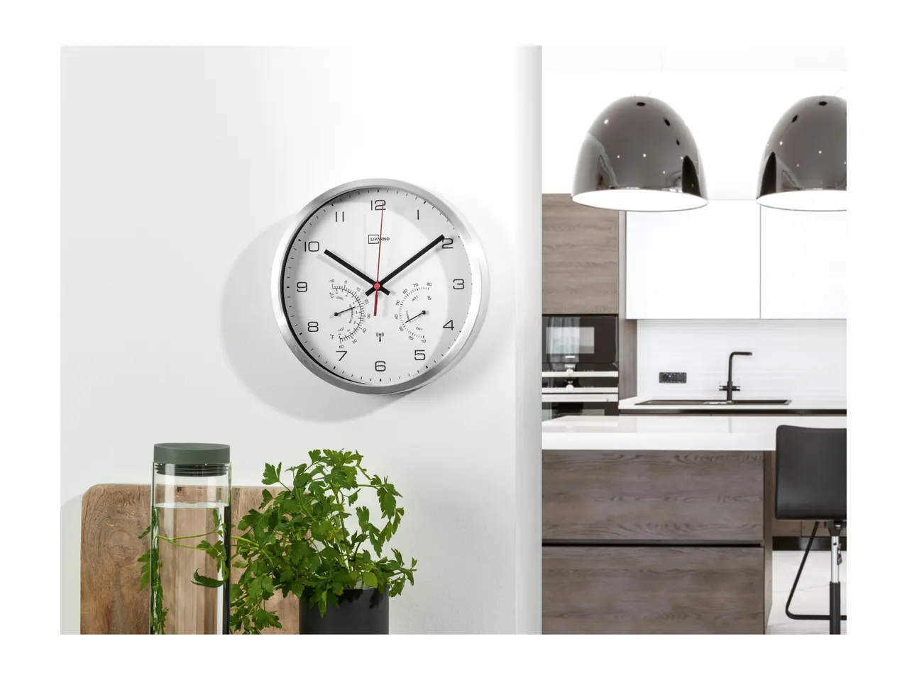 A silver wall clock with temperature and humidity displays, next to a modern kitchen.