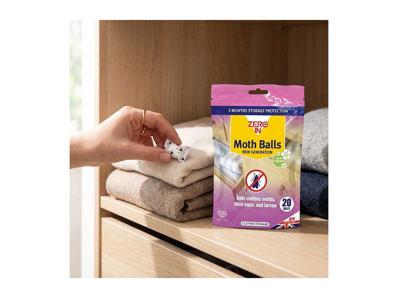 Hand placing a moth ball next to folded clothes, with a moth ball packaging on the right.