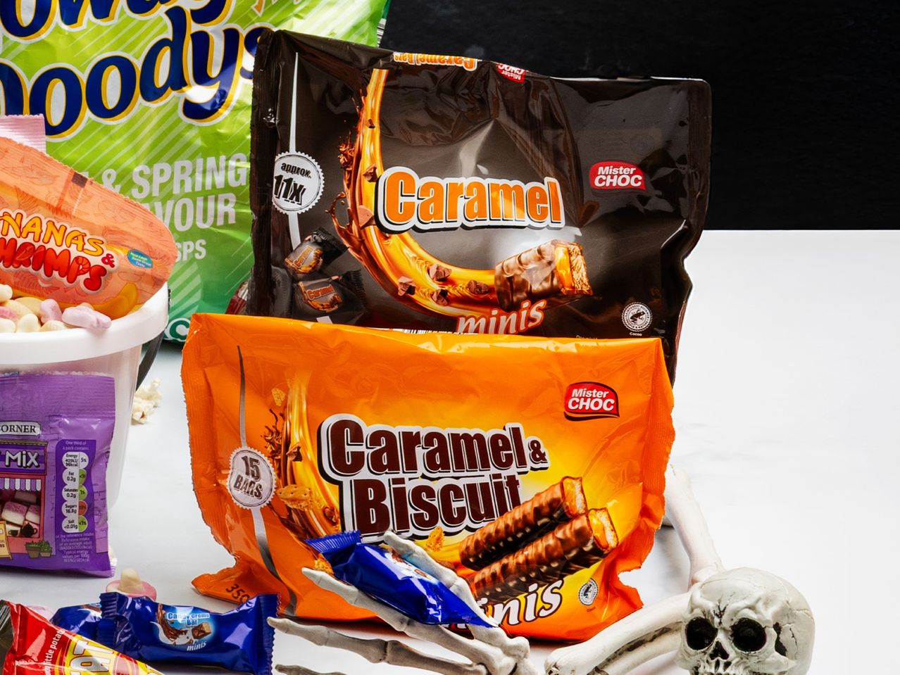 Halloween candy assortment with caramel chocolate bars, gummy sweets, and a skeleton hand.