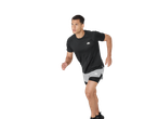 Man in black short-sleeved sports top and grey and black sports shorts running.