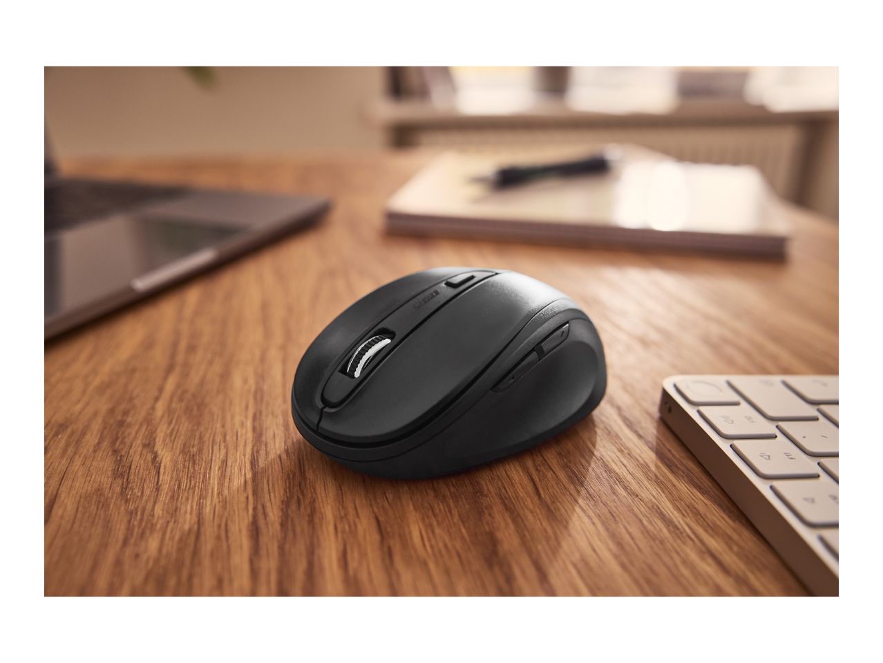 Black computer mouse on a wooden desk with a laptop and keyboard in the background.