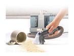 Handheld spot cleaner removing a coffee spill from a white carpet next to an overturned mug.