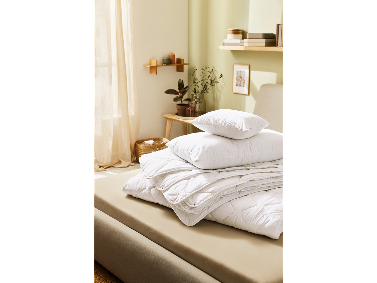 A neatly folded white duvet and pillows sit on a beige bed in a minimalist bedroom.