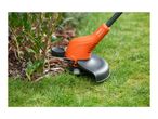 Orange grass trimmer cutting grass next to a green bush.