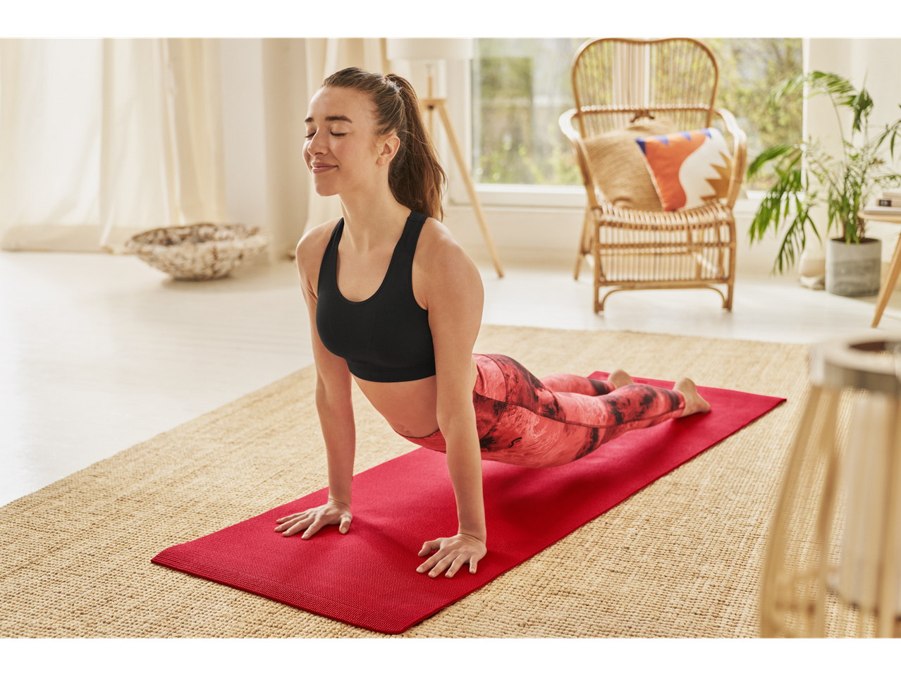 Femeie făcând yoga în poziția de cobra pe un covor roșu.