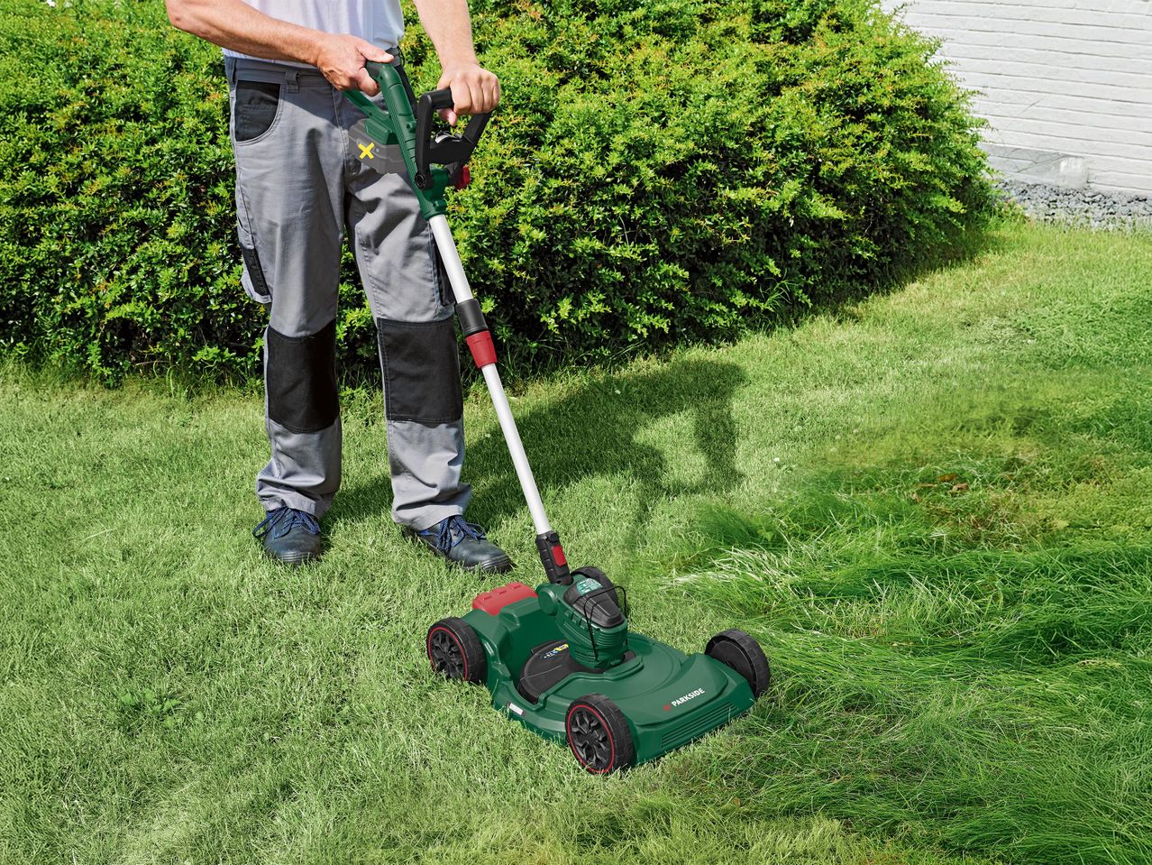 Férfi akkumulátoros fűnyíróval vágja a füvet a kertben.
