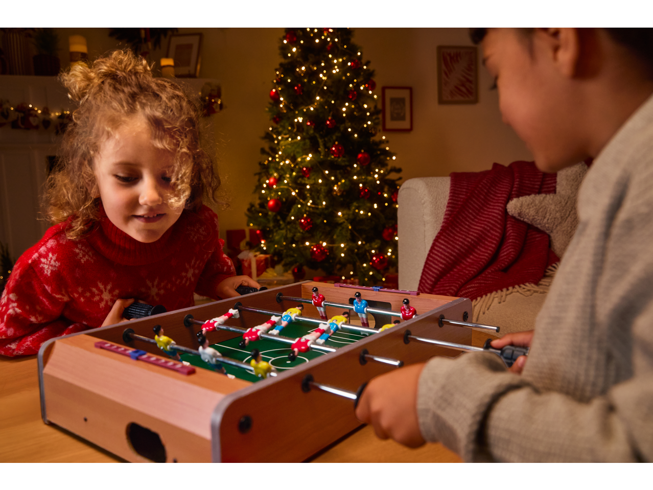 Two children playing with a Lupilu tabletop foosball game near a Christmas tree.