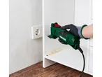 Una persona che indossa guanti neri usa un utensile multifunzione verde per tagliare un ripiano bianco.