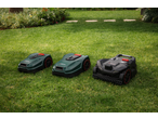 Three robotic lawnmowers, two green and one black, on a lush green lawn.