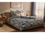 A beige bed with a navy blue floral duvet cover and matching pillows sits in a sunlit bedroom.
