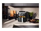 A modern air fryer on a kitchen countertop next to prepared food and kitchen accessories.