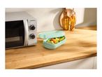 A microwave and a light green food container with vegetables on a wooden kitchen counter.