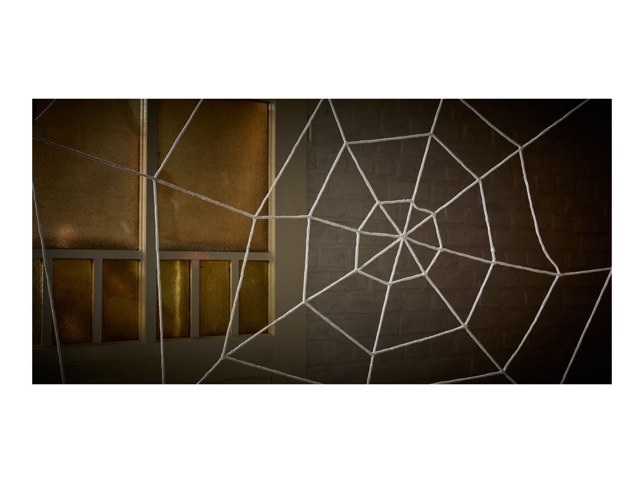 A white spiderweb stretches across a window with golden panes and a brick wall.