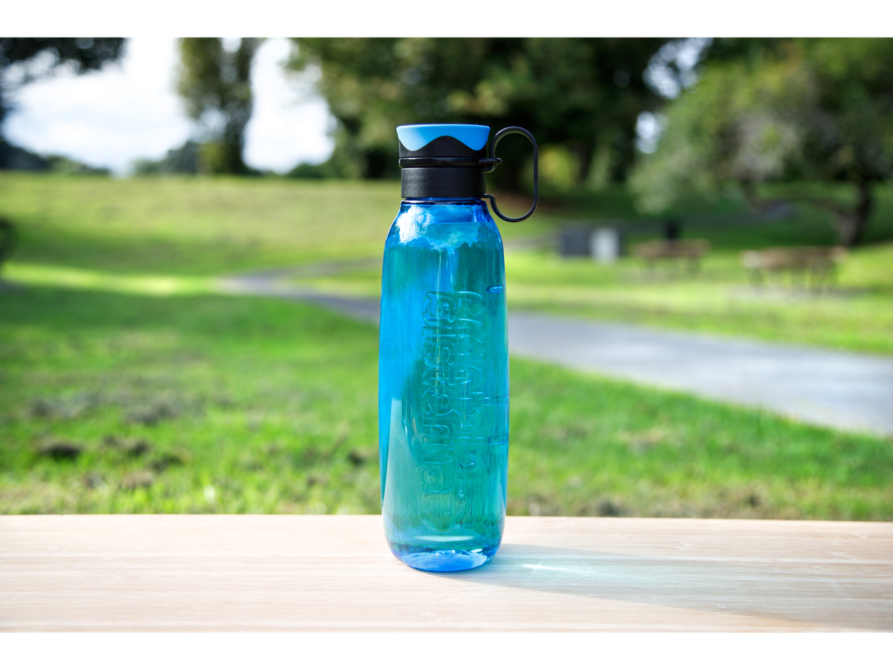 Sistema blue drinks bottle on a wooden surface with a blurred green park in the background.