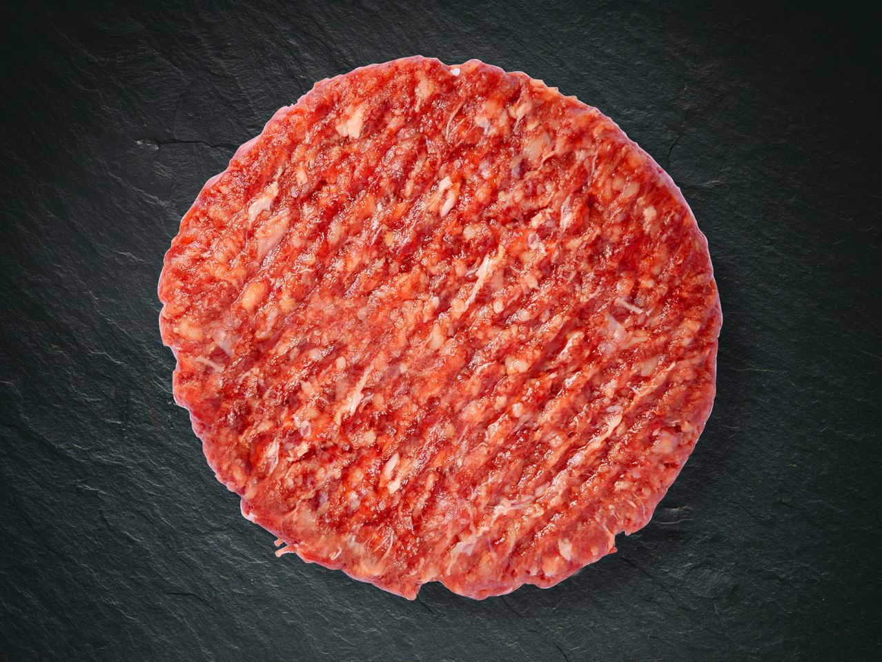 Un steak haché cru, rond, sur un fond noir.