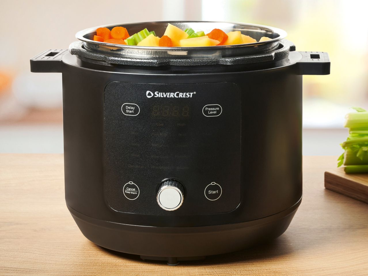 A black Breville pressure cooker sits on a kitchen counter with cooked vegetables inside.