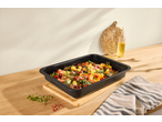 Baked gnocchi with vegetables and herbs in a black baking dish on a wooden counter.
