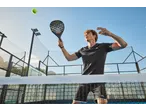 Homem em roupa desportiva com raquete de padel e bola num campo.