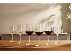 Șase pahare de vin, două pentru vin alb și patru pentru vin roșu, pe o masă din lemn.
