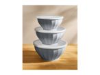 Stack of three grey mixing bowls with white lids on a wooden surface.