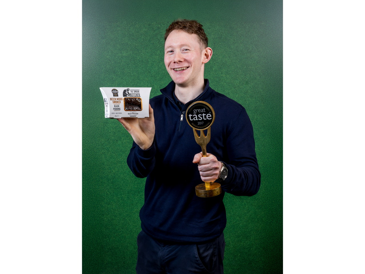 Man holding a 'Great Taste 2017' award and 'The Smokin' Butcher' black pudding.