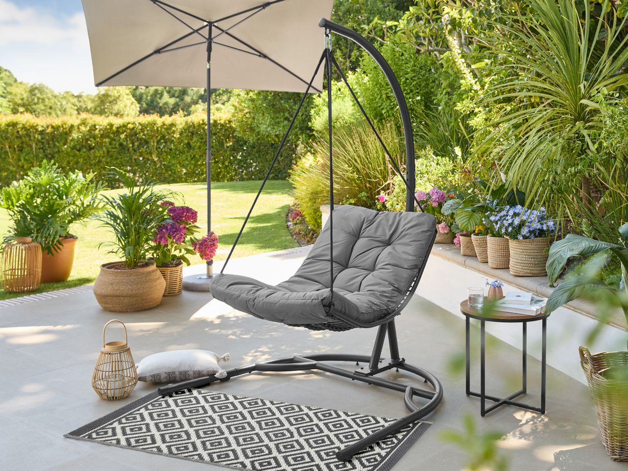 Outdoor patio with a grey hanging chair, umbrella, potted plants, and a small side table.