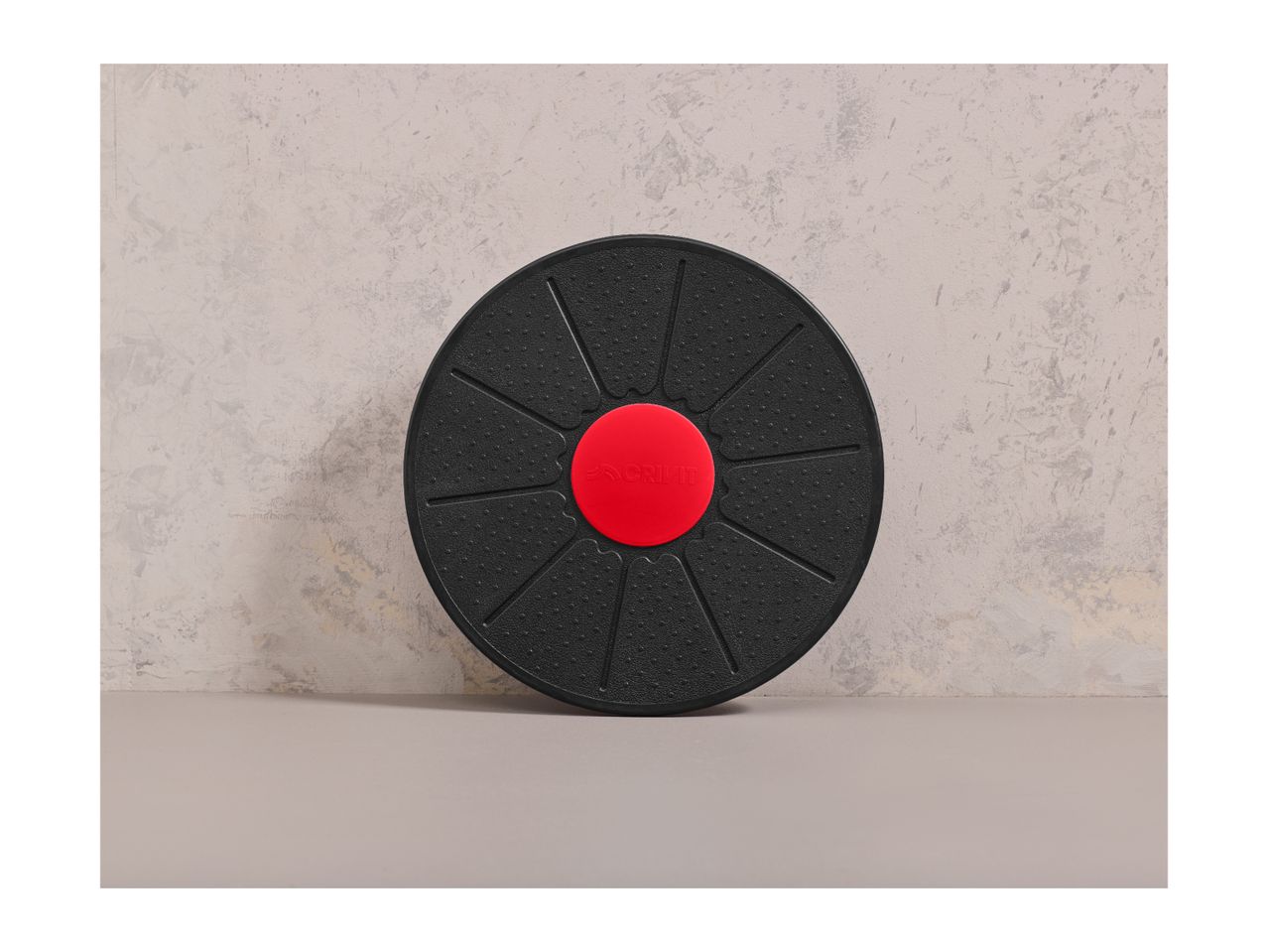 A black balance board with a red center, featuring the Crivit logo, against a textured wall.