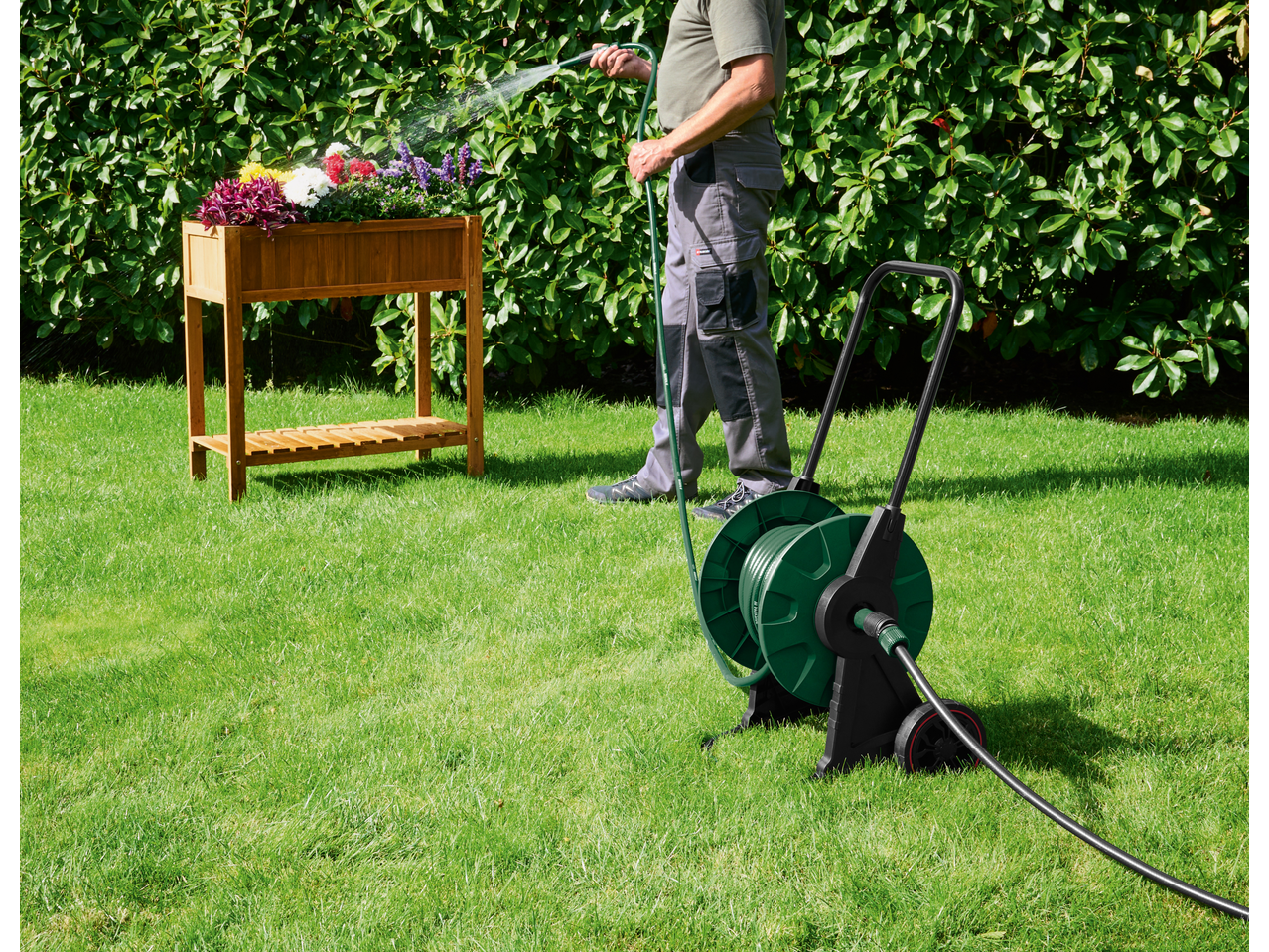 Cărucior pentru furtun PARKSIDE cu un bărbat udând flori într-o jardinieră de lemn.