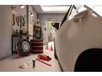 Garage scene with a white car, tyre pressure gauge, car jack, and stacked tyres.