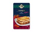 Lasagne alla Siziliana med oksekød på en hvid tallerken, omgivet af tomater.