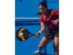 Mulher a jogar padel com raquete e bola num campo azul.