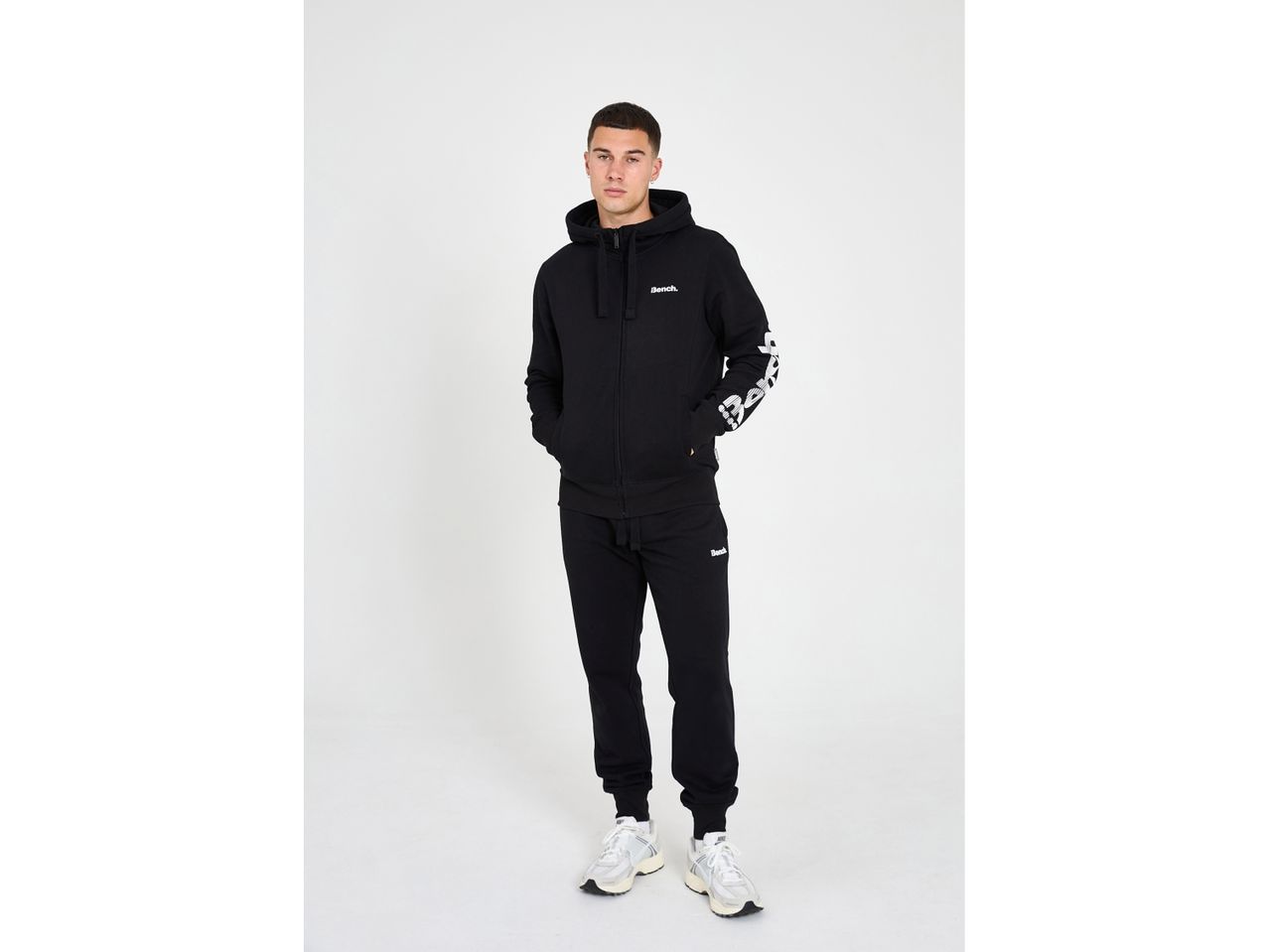 Uomo in tuta nera Bench con felpa con cappuccio e pantaloni della tuta, scarpe da ginnastica bianche.