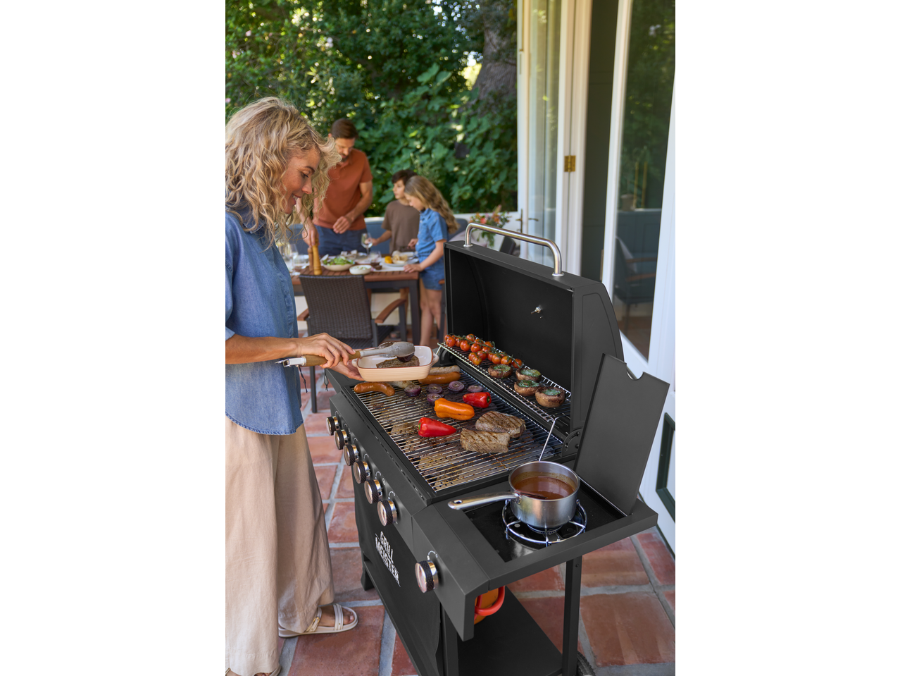 Woman grilling on a Grillmeister 6 Burner Gas Barbecue with family in the background.