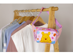 Bolsa de cintura rosa do Winnie the Pooh com flores, pendurada num cabide de madeira.