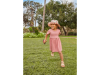 A happy child in a pink dress and heart-patterned sun hat runs on a grassy lawn.