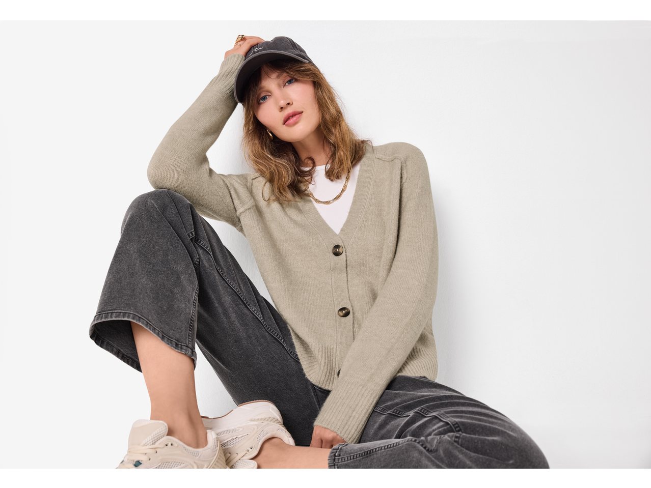 Woman in esmara® chunky knit cardigan, white t-shirt, dark jeans, and cap.
