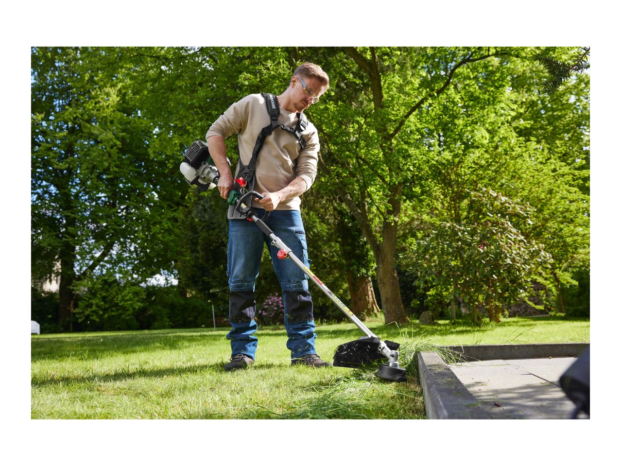 Man using a petrol brush cutter to trim grass in a garden.