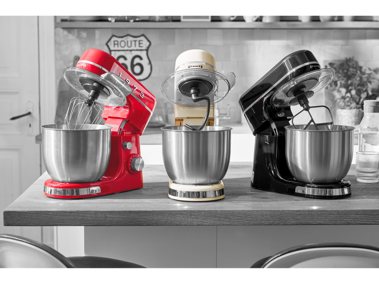Three stand mixers in red, cream, and black on a kitchen counter with a Route 66 sign.