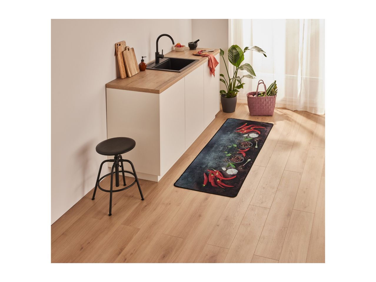A modern kitchen with a black sink, wooden countertop, and a chili-themed kitchen mat.