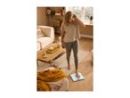 Woman stepping on a bathroom scale in a living room with a sofa and coffee table.